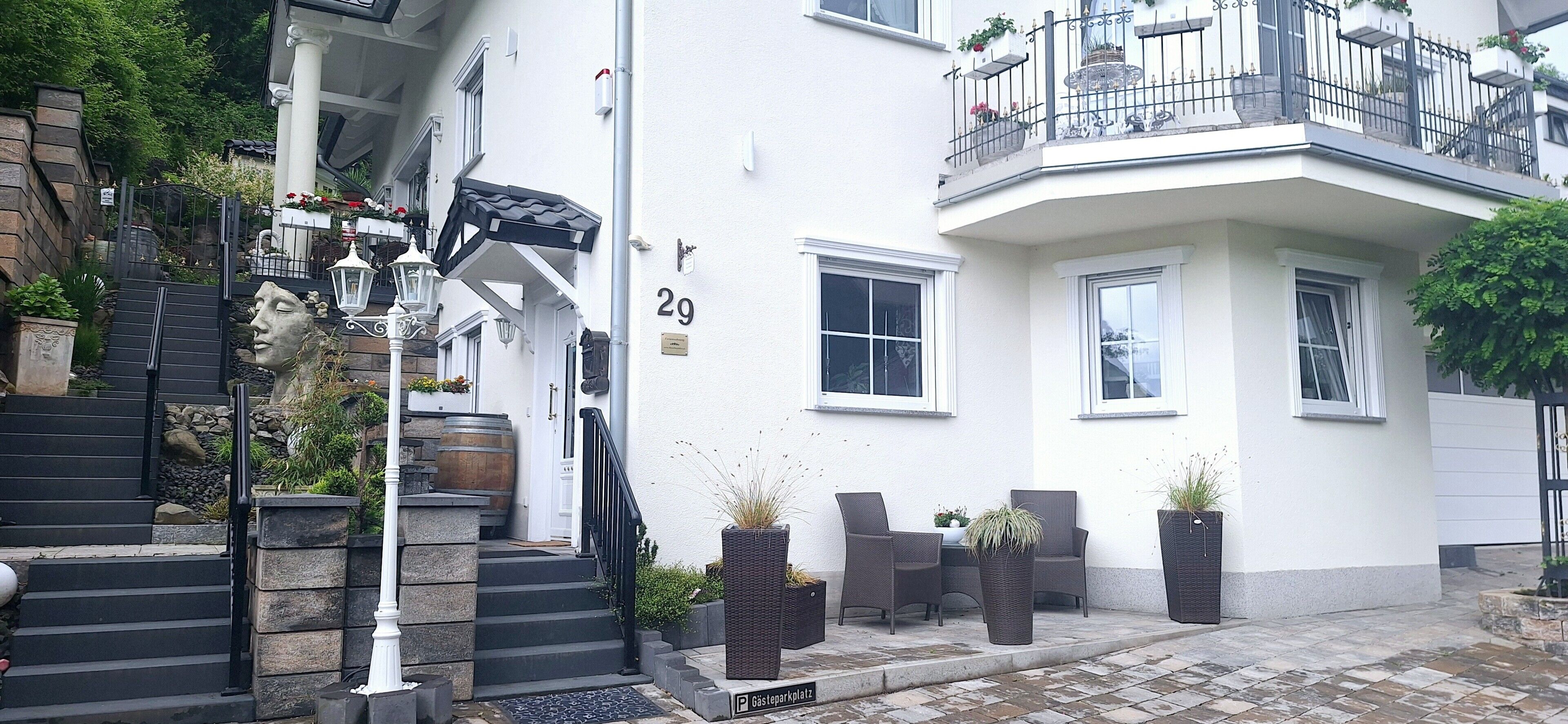 Ein weißes Gebäude mit Balkon, Treppe und Außenbereich mit Sitzgelegenheiten.