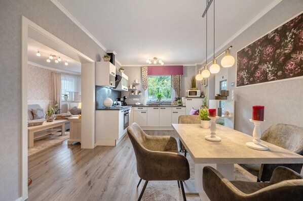 A modern kitchen with white cabinets, a dining area with a table and chairs, and a view of the outdoors through a window.