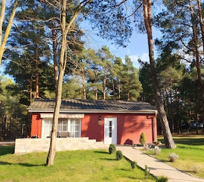 Ett rött, enplanshus med en veranda på framsidan, en liten trädgård framför huset och en uppfart.