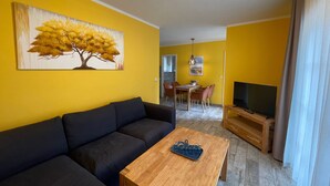 Een woonkamer met een bank, een salontafel, een televisie en een schilderij aan de muur.