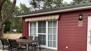 A red building with a covered patio, a table with chairs, and a window with a white frame. - Holiday Home 'Eichelhäher' with Private Terrace, Private Garden and Wi-Fi (Zossen)