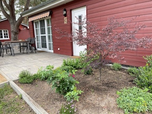 Ein rotes Holzhaus mit Terrasse, Sitzgelegenheit im Freien und einem Garten mit verschiedenen Pflanzen.