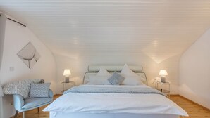 A bedroom with a bed, a chair, two bedside tables with lamps, and a wall-mounted light fixture.