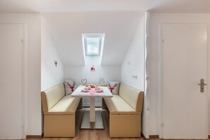 Une pièce avec une table blanche, un canapé beige, une petite fenêtre et une porte.