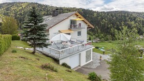 A two-story house with a balcony, a garage, and a view of a forested hillside.