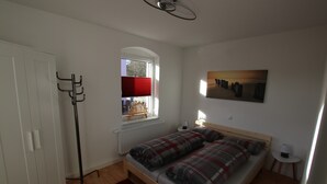 A bedroom with a bed, a window with a red blind, a radiator, a coat rack, and a painting on the wall. - Apartment 'Ferienwohnung Am Bärenstein' with Balcony and Wi-Fi (Bärenstein)