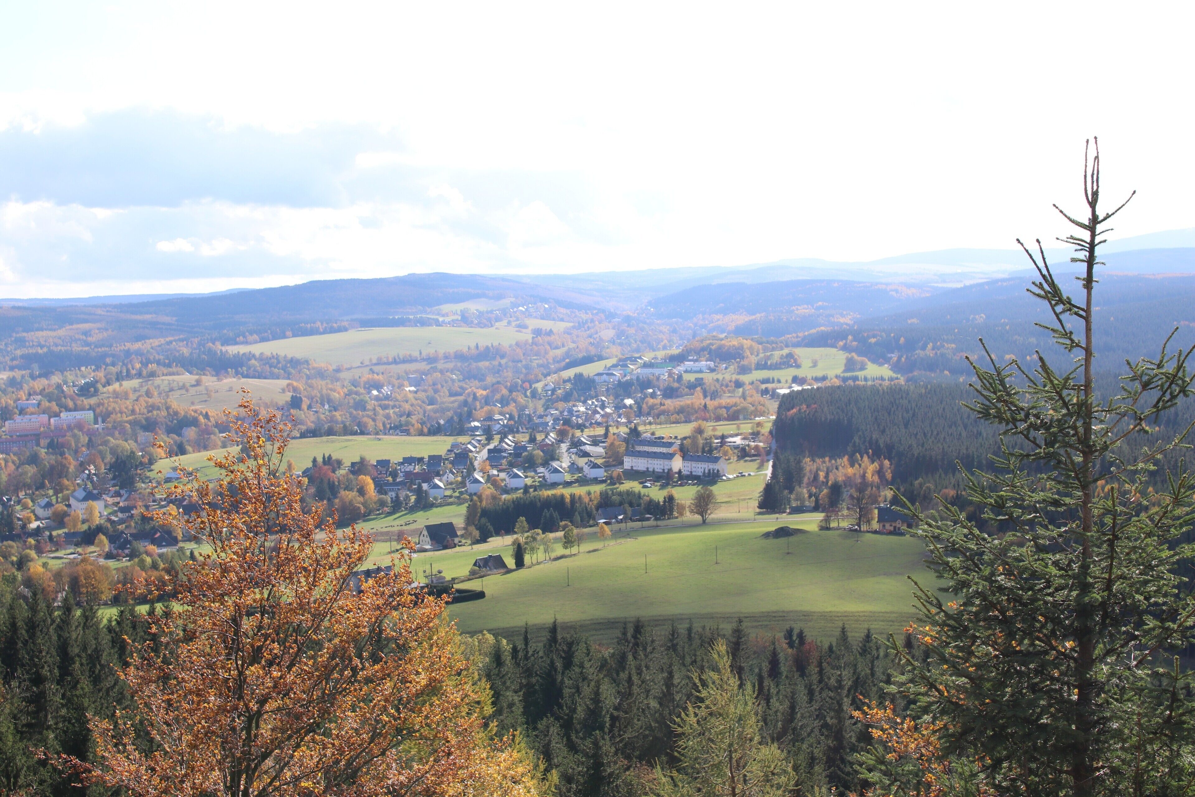 Ein weites Panorama einer Stadt, eingebettet in ein Tal, umgeben von Hügeln und Wäldern.