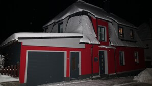 A two-story building with a red exterior and a garage door. - Apartment 'Ferienwohnung Am Bärenstein' with Balcony and Wi-Fi (Bärenstein)