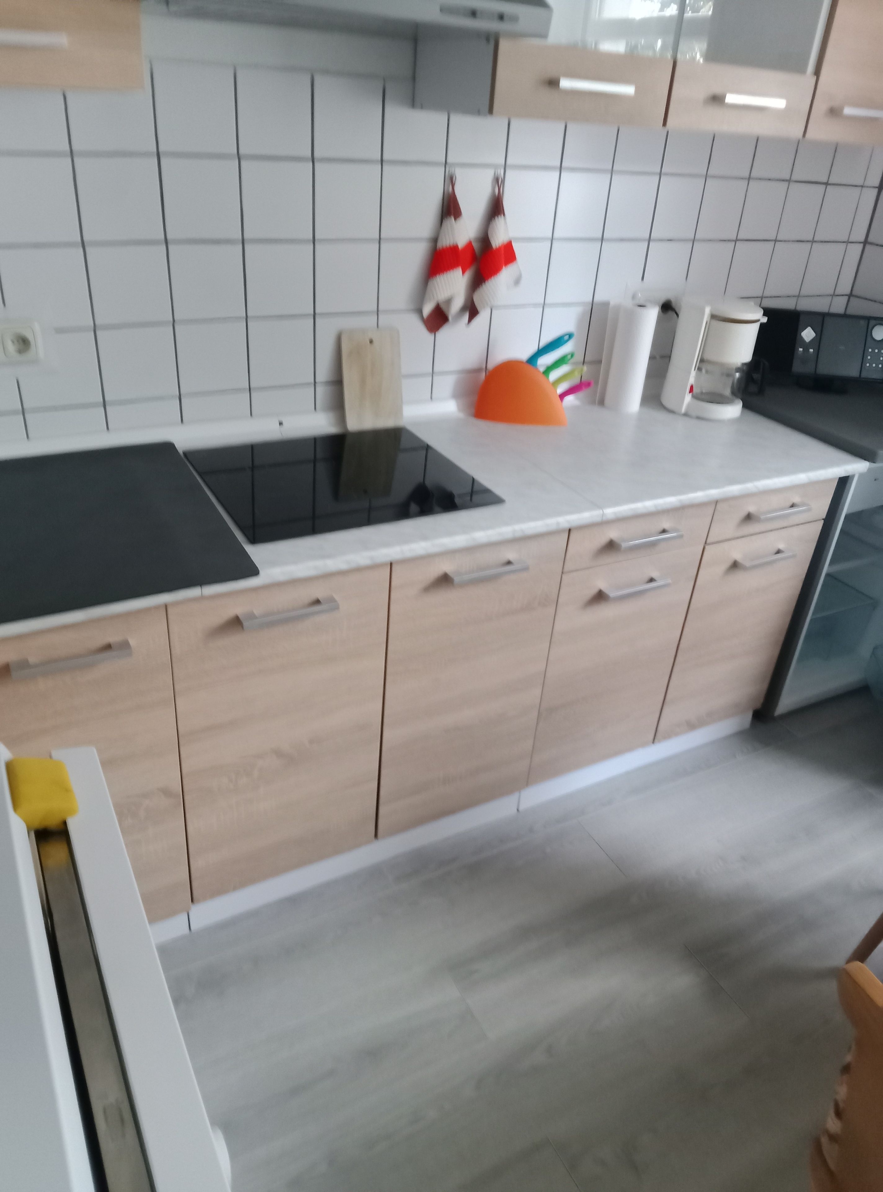 A kitchen with a black induction cooktop, wooden cabinets, a white countertop, and a coffee maker.