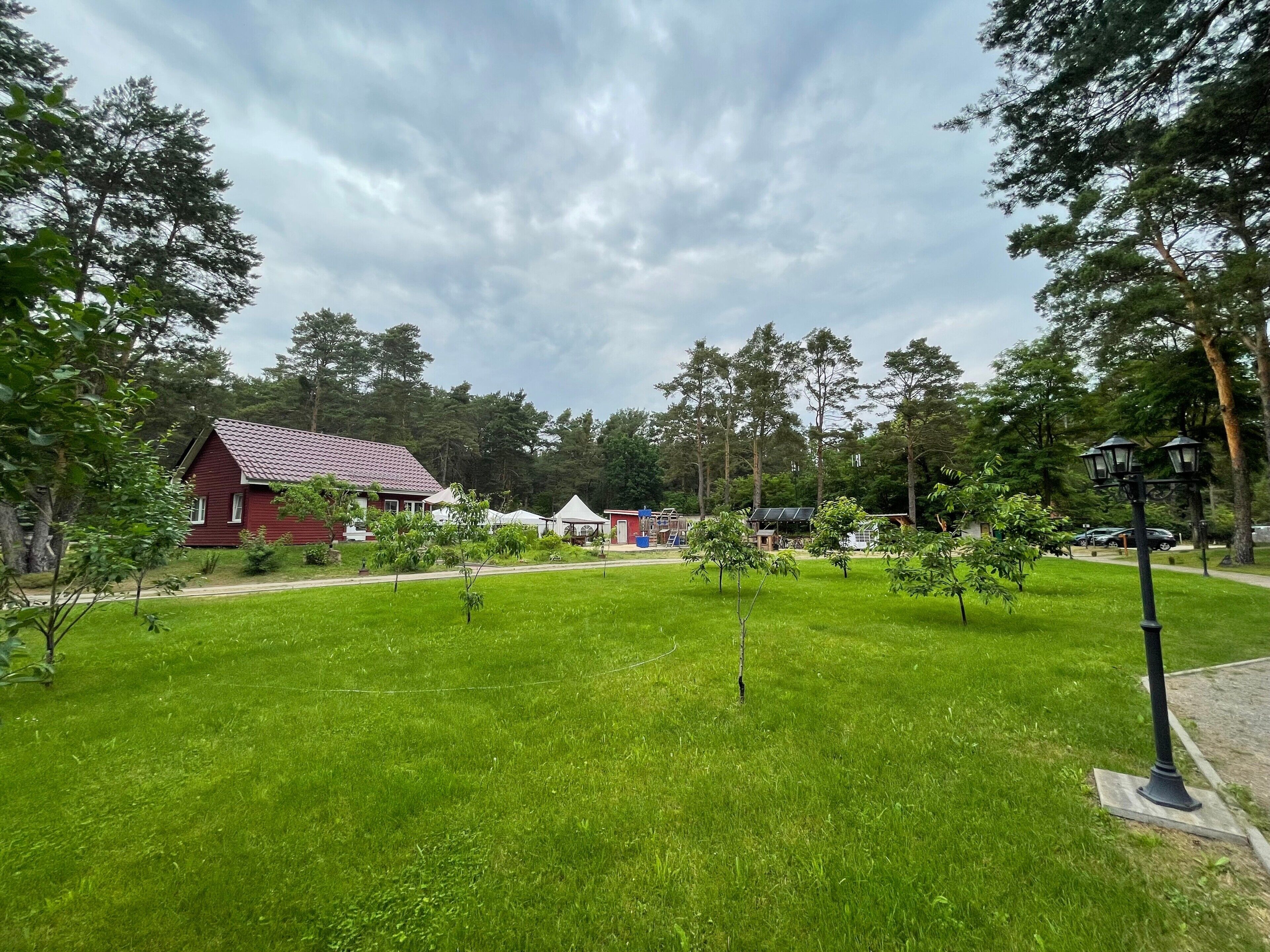 Une zone herbeuse avec un bâtiment rouge, des arbres et un lampadaire.
