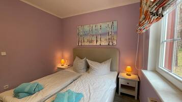 A bedroom with two beds, a nightstand with lamps, a painting on the wall, and a window with curtains.