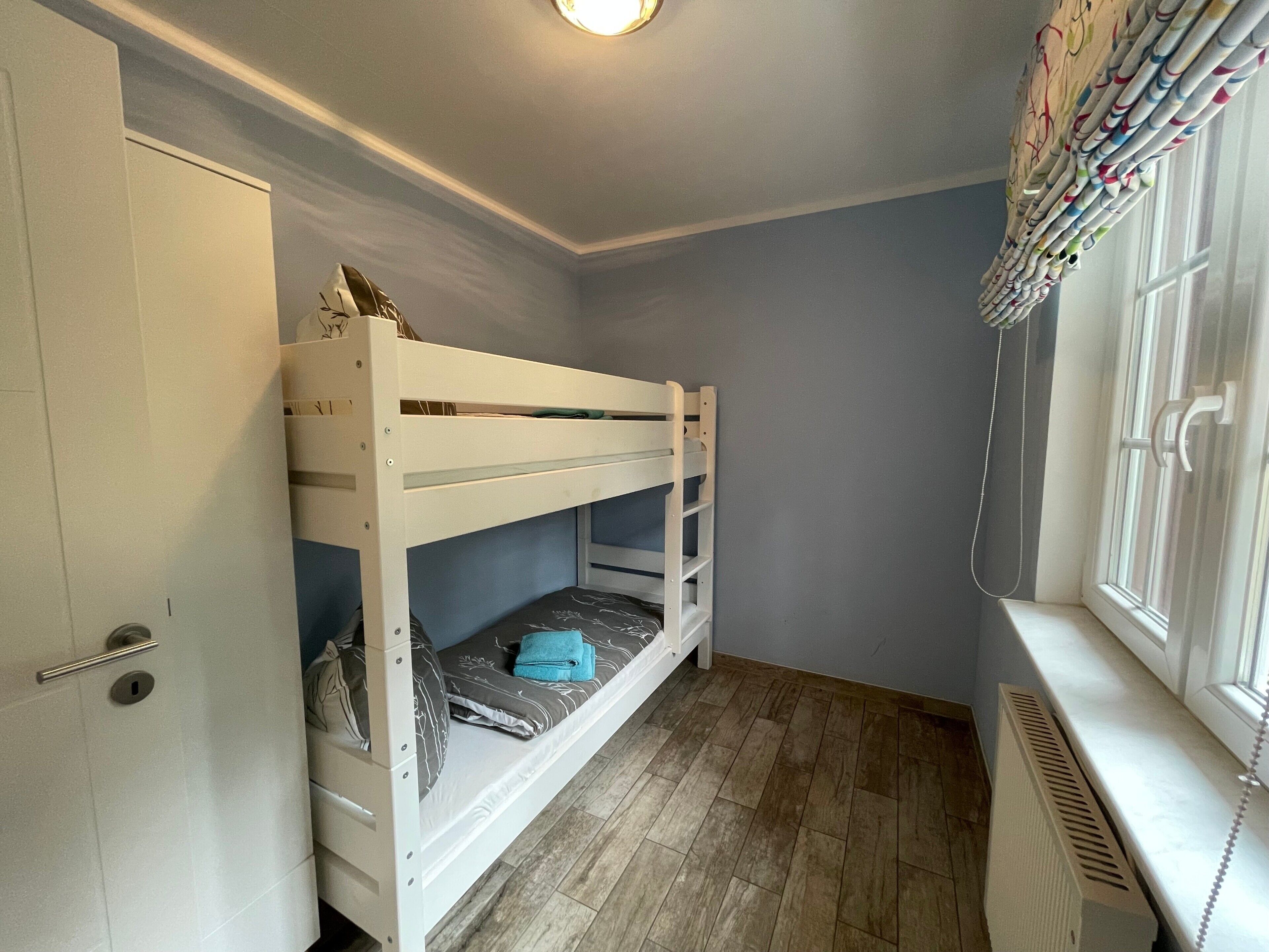 A bunk bed in a room with a door, a radiator, and a window with curtains.