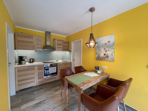 A kitchen with wooden cabinets, a tiled backsplash, a coffee maker, and a dining area with a table and chairs. - Holiday Home 'Eichhörnchen' with Private Terrace, Private Garden and Wi-Fi (Zossen)