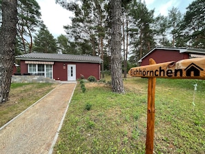 A wooden signpost with 'Eichhornchen' and a house symbol, a red building with a tiled roof, and a gravel path leading to it. - Holiday Home 'Eichhörnchen' with Private Terrace, Private Garden and Wi-Fi (Zossen)