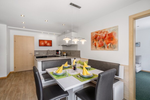 Un espace repas moderne avec une table blanche, des chaises noires et un set de table vert.
