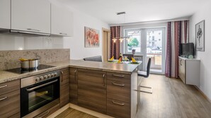 A modern kitchen with a built-in oven, a large island with a sink, and a dining area with a chair. - Holiday Apartment "Nr 2 Haus Voglreiter" with Mountain View, Shared Garden & Wi-Fi (Kaprun)