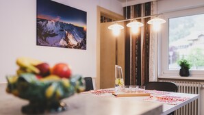 A dining area with a table, chairs, a fruit bowl, a pitcher with a glass, and a window with a view. - Holiday Apartment "Nr 2 Haus Voglreiter" with Mountain View, Shared Garden & Wi-Fi (Kaprun)