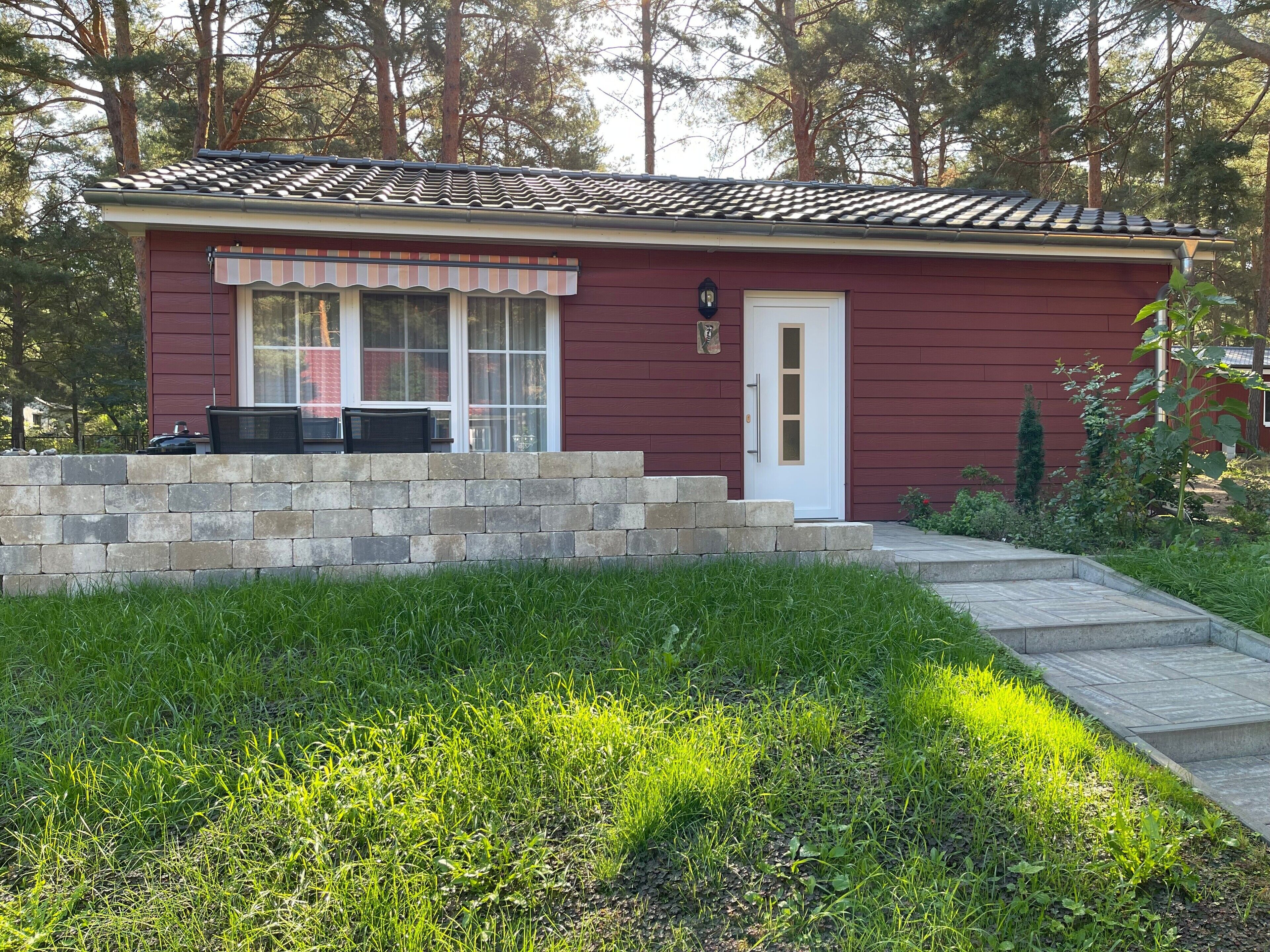 A small, single-story building with a red exterior, a white door, and a stone wall in front.