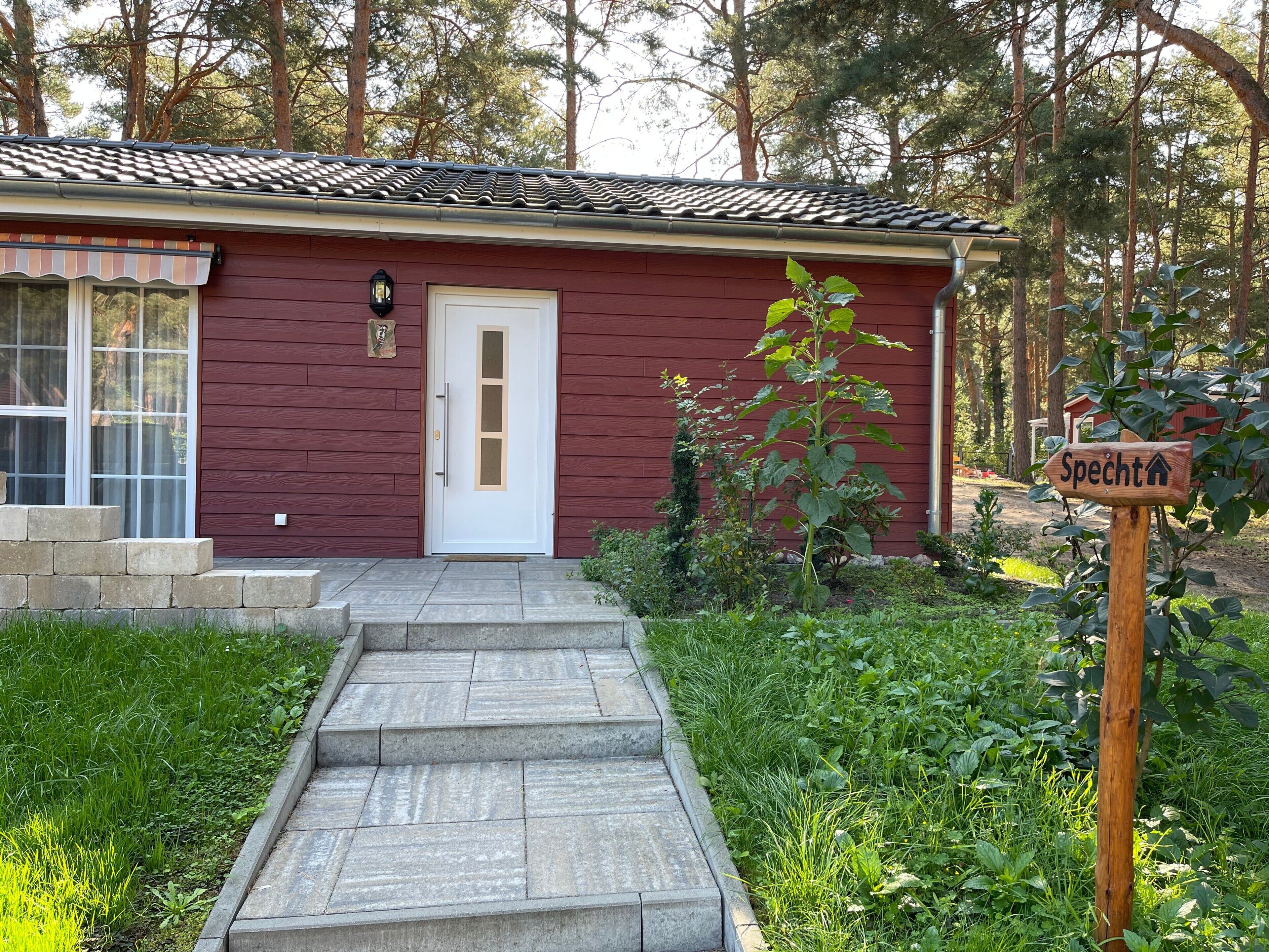 A red building with a white door, a small garden, and a sign that reads 'Specht'.
