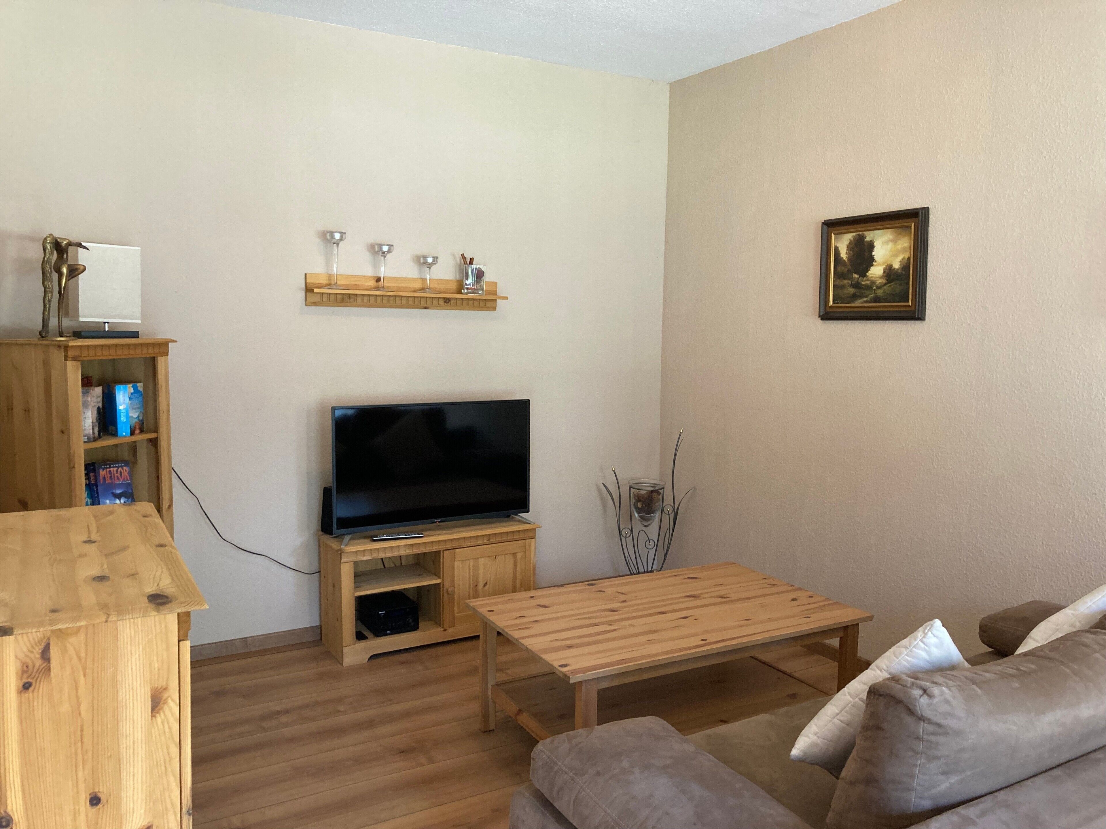 A living room with a TV, wooden furniture, a bookshelf, and a painting on the wall.