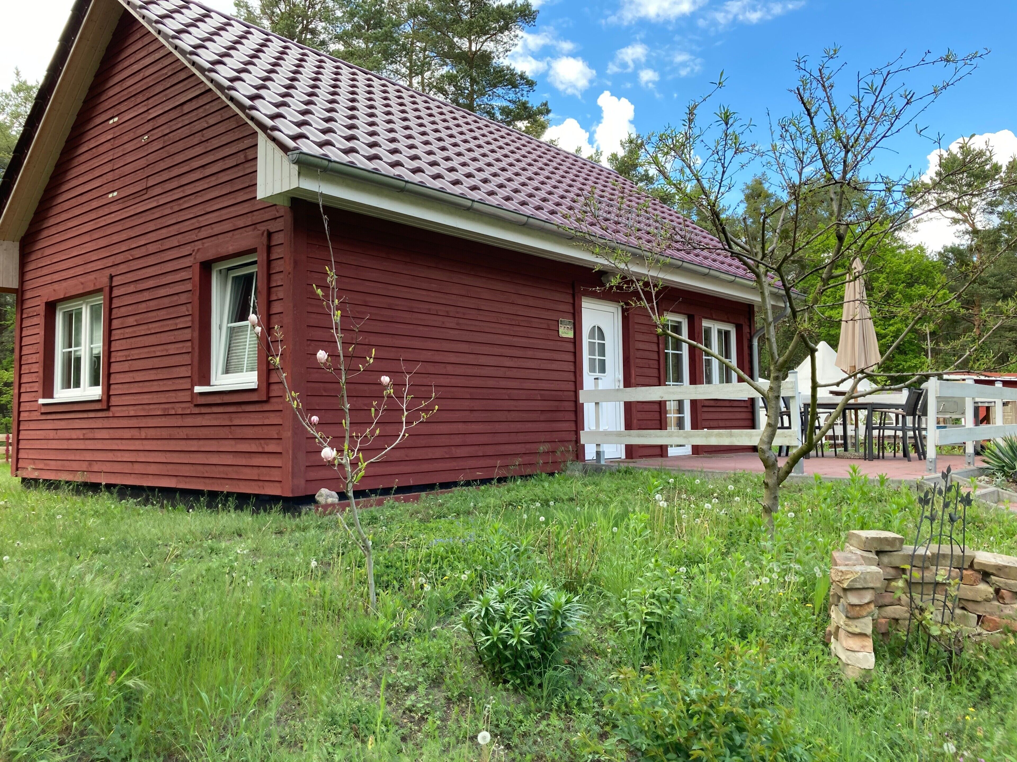 En rød træbygning med tegltag, en hvid veranda og en stenvæg.