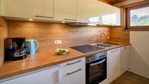 A modern kitchen with wooden cabinets, a black stove, a sink, and a window with a view of greenery.