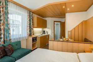 A compact room with a kitchenette, a sofa, a bed, and a mirror.