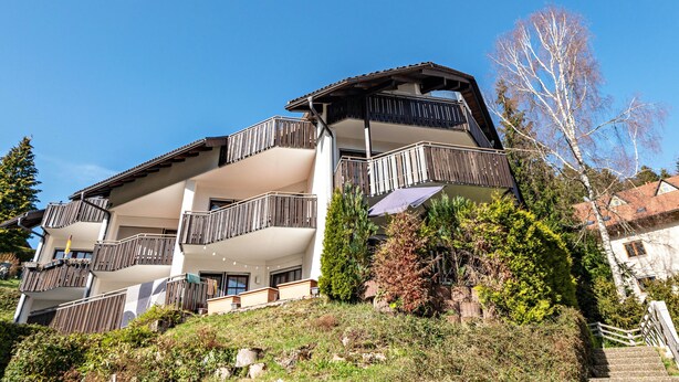 A multi-story building with balconies, a sloped roof, and a flag.