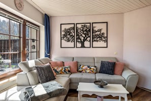 A living room with a sectional sofa, a small white table, and a window with curtains.