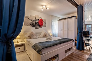 Une chambre à coucher comprenant un lit, des tables de chevet, une œuvre d’art murale, une armoire et un bureau avec une chaise.