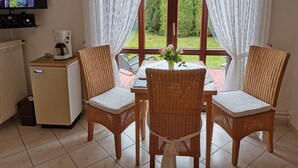 Un comedor con sillas de mimbre, una mesa con un jarrón de flores y una cafetera sobre un mueble.