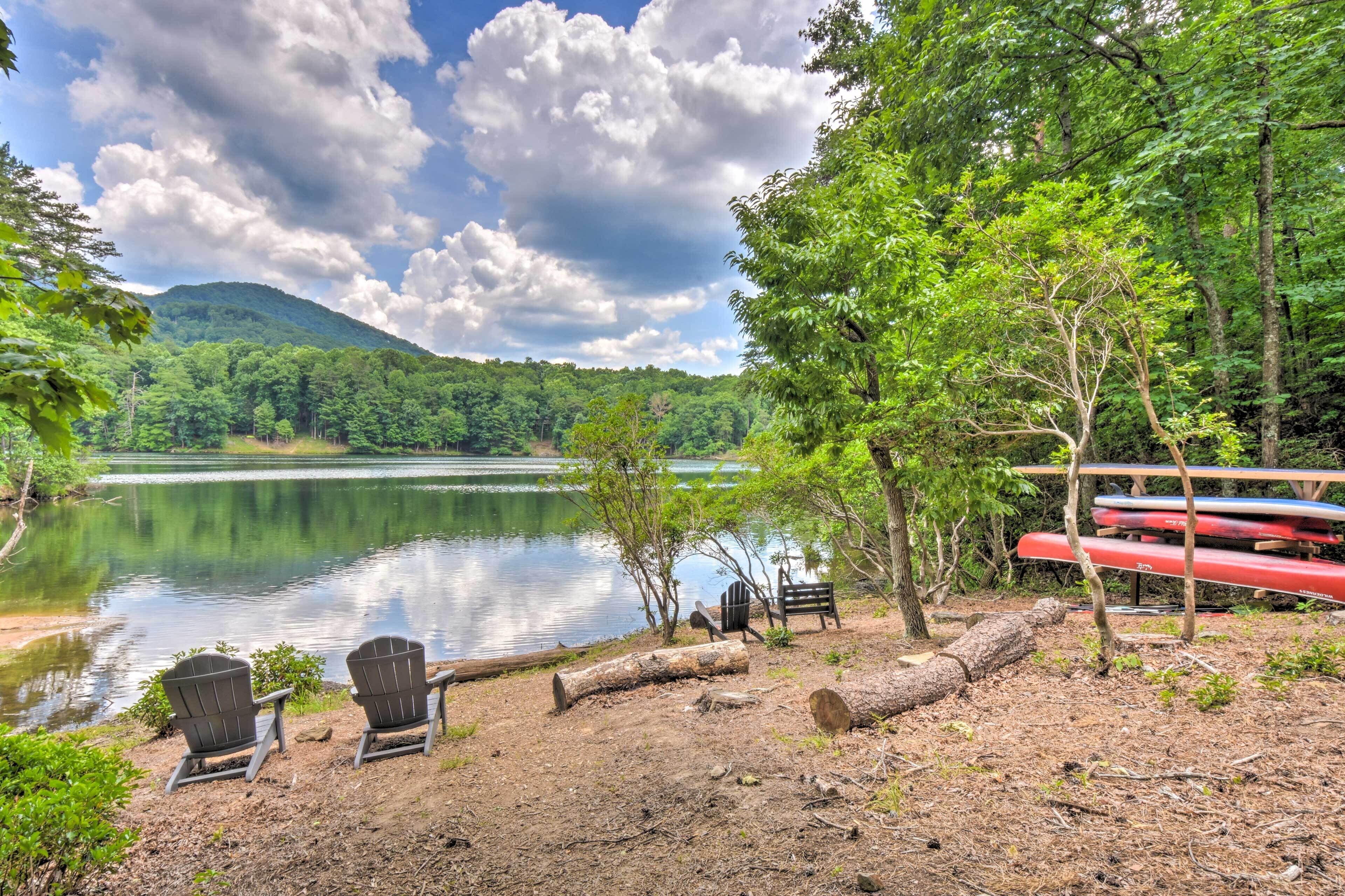 A lakeside view with two Adirondack chairs, a bench, and a canoe rack.