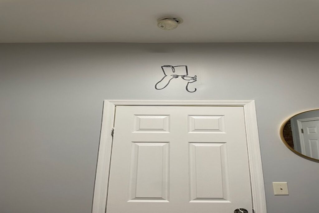A white door with a simple, modern design, a small wall-mounted light fixture above it, and a round mirror on the adjacent wall.
