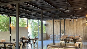 Un comedor interior con techos altos, vigas a la vista y una mezcla de mobiliario de madera y metal.
