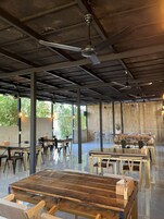 Un comedor interior con techos altos, vigas a la vista y una mezcla de mobiliario de madera y metal.