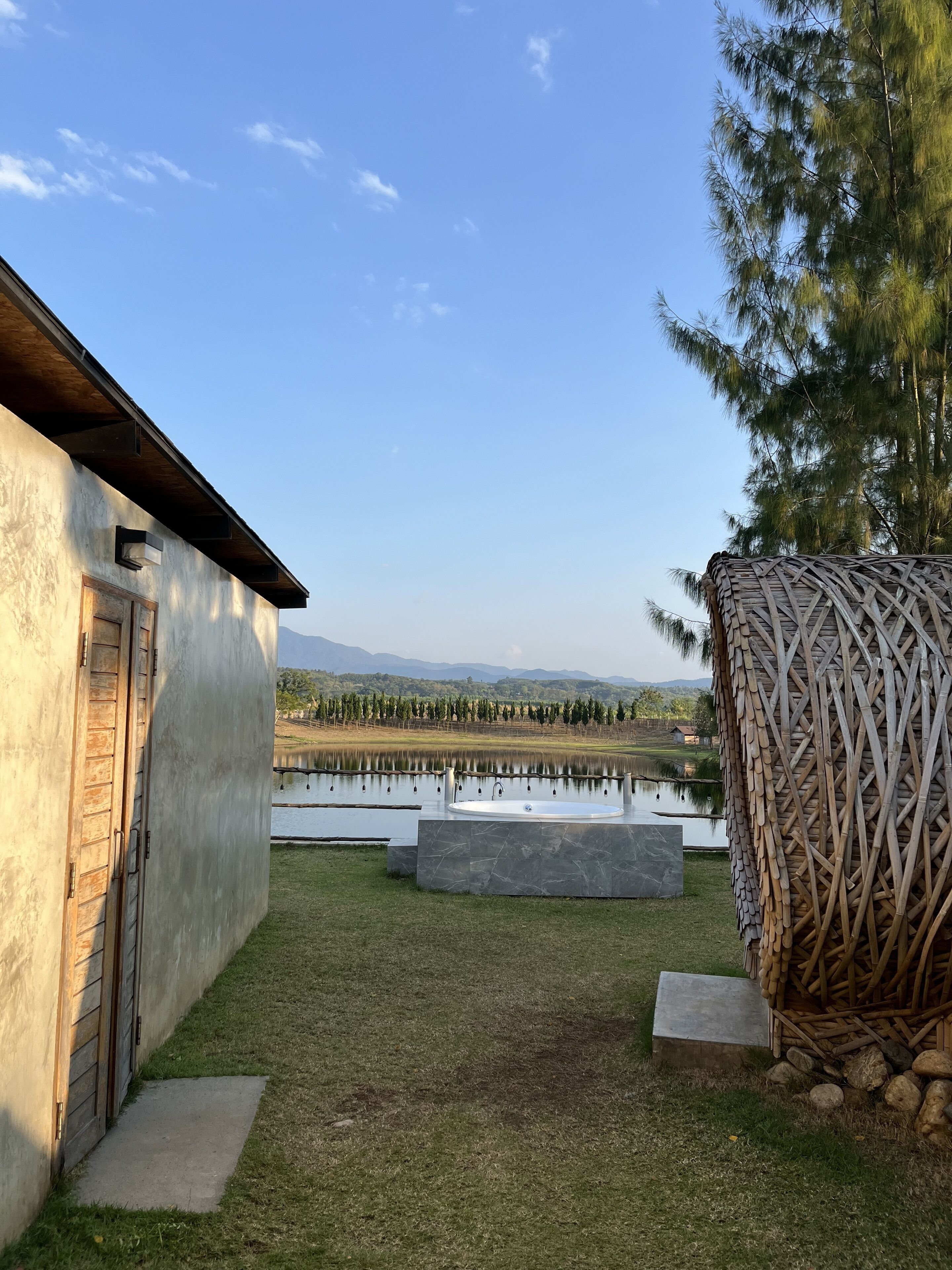 A rustic building with a wooden door, a stone bench, and a large woven structure.
