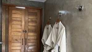 Un baño con puertas de madera, un perchero con albornoces blancos y suelo de mármol.