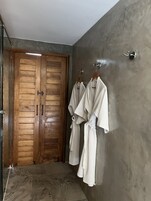 A bathroom with wooden doors, a towel rack with white robes, and a marble floor.