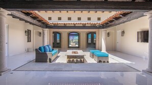 A spacious patio with a stone table and blue cushioned seating, surrounded by columns and a tiled ceiling.