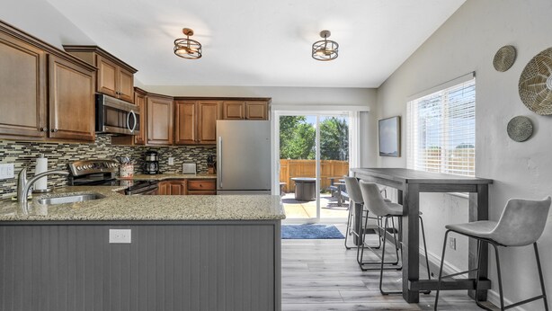 A modern kitchen with granite countertops, stainless steel appliances, and wooden cabinets. There is a bar area with stools and a large window providing natural light. - Park Place (Colorado Springs)