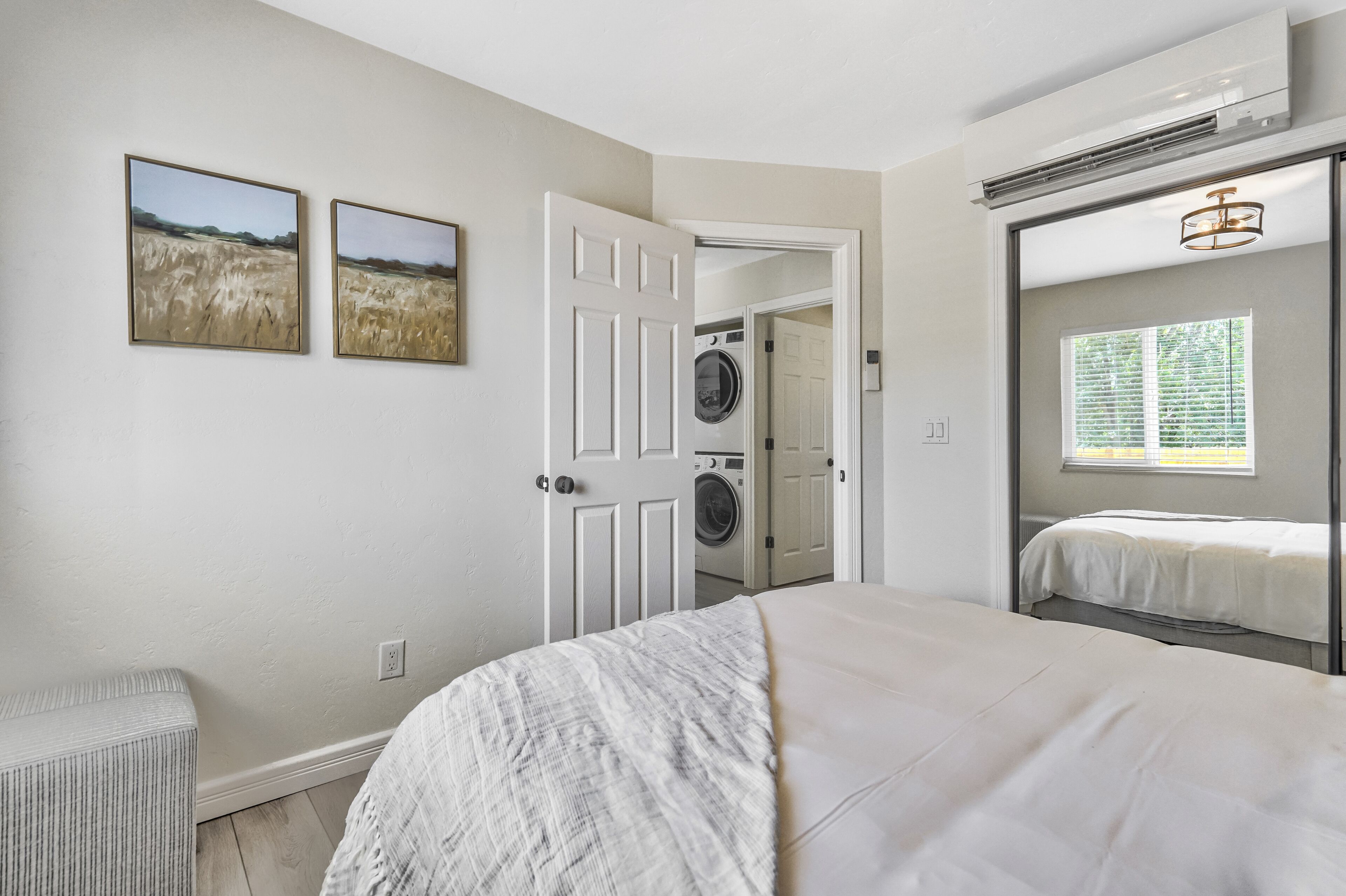 A bedroom with a bed, a bench, a door leading to a laundry room, and two wall-mounted pictures.