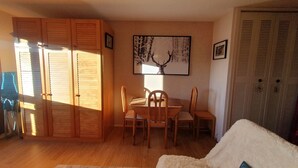 A room with a dining table, chairs, a sofa, and a wardrobe. - Studio Font-romeu Vue Imprenable Plein sud sur le Cambre D'aze ! (Font-Romeu-Odeillo-Via)