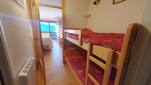 A room with bunk beds, a radiator, a door leading to a balcony, and a small table with chairs. - Studio Font-romeu Vue Imprenable Plein sud sur le Cambre D'aze ! (Font-Romeu-Odeillo-Via)