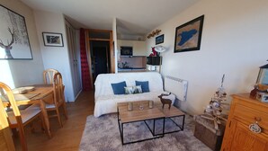 A cozy room with a bed, a wooden dining table, chairs, a fluffy rug, a small coffee table, and a dresser. - Studio Font-romeu Vue Imprenable Plein sud sur le Cambre D'aze ! (Font-Romeu-Odeillo-Via)