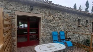Ein Gebäude aus Stein mit einer Holzterrasse, einer roten Tür und blauen Stühlen.