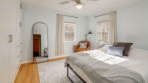 A bedroom with a bed, a ceiling fan, a wardrobe, two windows with curtains, and a mirror. - Central Rapid City Home w/ Sunroom & Fireplace! (Rapid City)