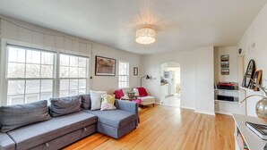 A spacious living room with a grey sectional sofa, a small white table, and a wooden floor. - Central Rapid City Home w/ Sunroom & Fireplace! (Rapid City)