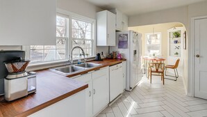 A kitchen with white cabinets, a wooden countertop, a sink, and a dining area with a table and chairs. - Central Rapid City Home w/ Sunroom & Fireplace! (Rapid City)