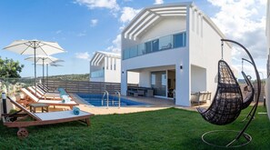 A modern house with a swimming pool, outdoor seating, and a hanging chair.
