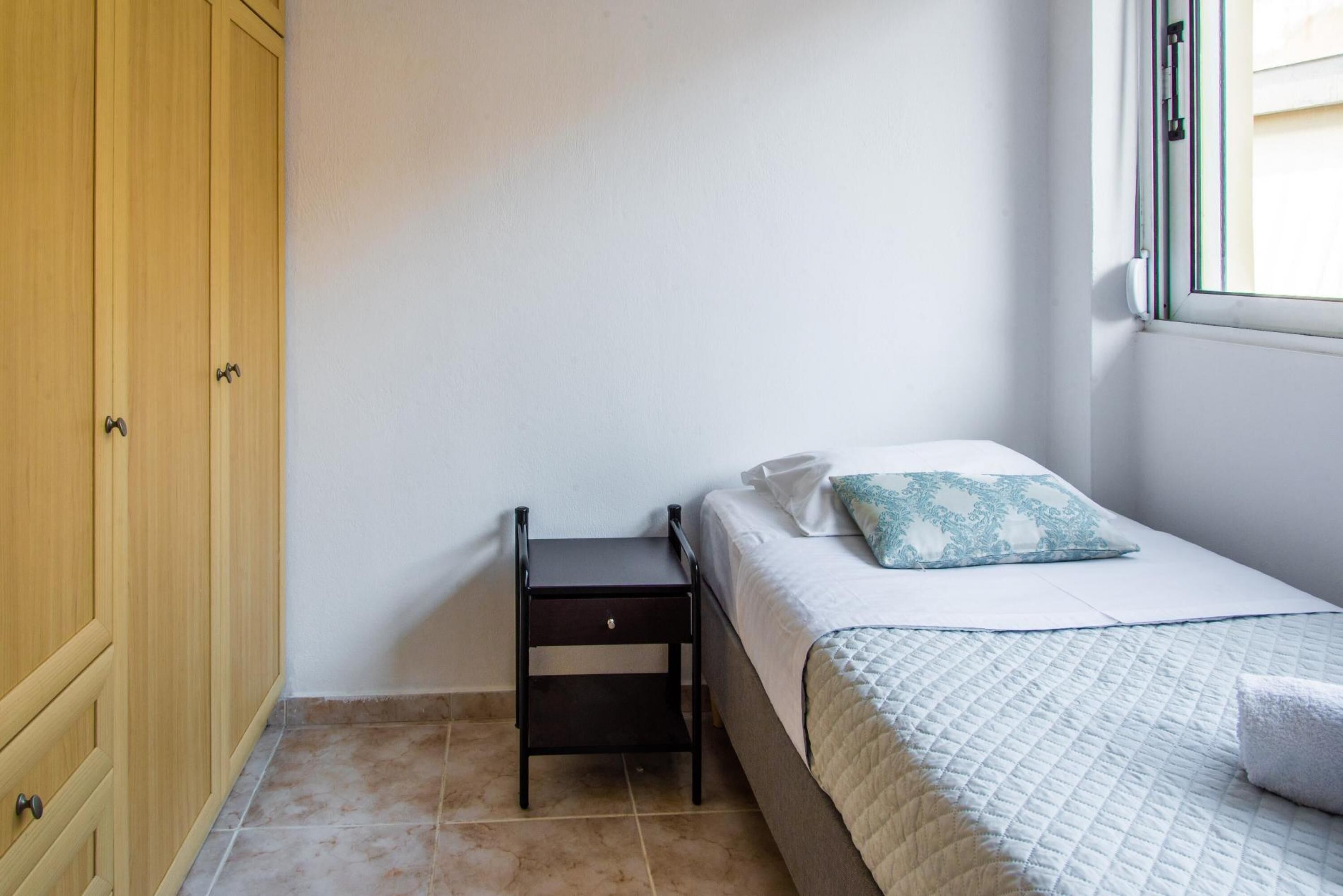 Un dormitorio pequeño y ordenado con una cama, una mesita de noche y un armario.